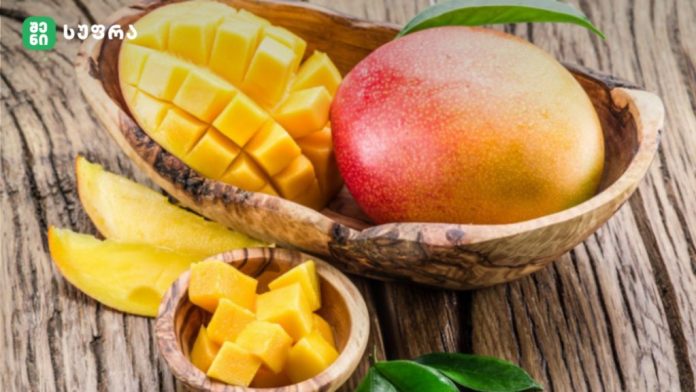 Ripe mango halves cut into cubes in a wooden bowl on a rustic wooden surface of weathered planks.