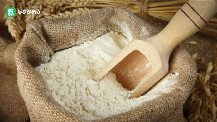 Open burlap sack filled with white flour with a wooden scoop resting inside.