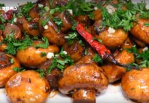 Სოკოს ცხარე კერძი Close-up of round, glazed mushrooms (or small potatoes) in a rich brown sauce, sprinkled with chopped parsley and a red chili pepper for garnish.