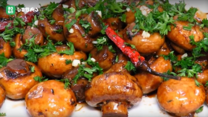 Close-up of round, glazed mushrooms (or small potatoes) in a rich brown sauce, sprinkled with chopped parsley and a red chili pepper for garnish.