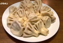 ხინკალი – ქართული სუფრის მშვენება Plate of steamed dumplings with pleated edges arranged in a circle on a white plate atop a wooden table.