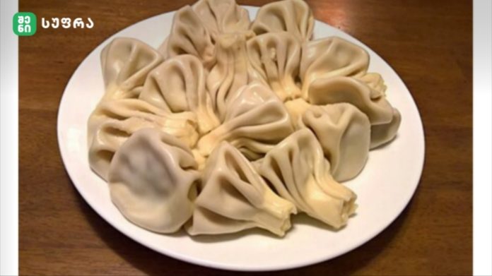 Plate of steamed dumplings with pleated edges arranged in a circle on a white plate atop a wooden table.