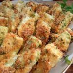 Plate of golden-brown breaded, herb-crusted fried sticks with a side of creamy dipping sauce and parsley garnish.