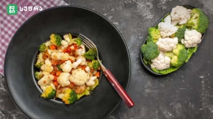 Black bowl with cauliflower, broccoli and carrot vegetables in sauce; red-handled fork; side plate of broccoli and cauliflower on a dark surface