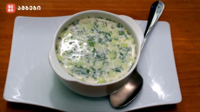 Creamy green herb soup in a white bowl on a pale plate with a spoon beside it; garnished with chopped greens.