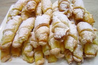 Pile of powdered-sugar-dusted crescent pastries arranged on a white serving tray/plate.