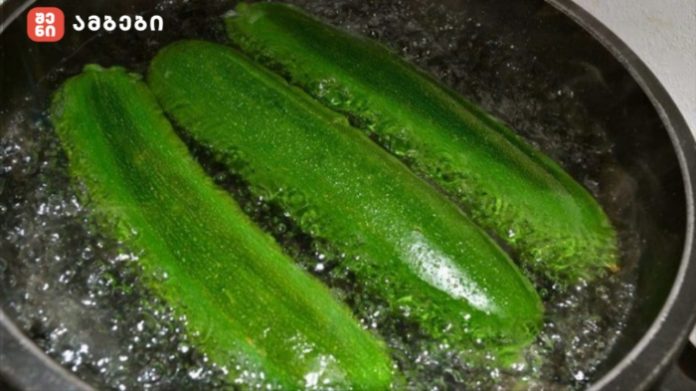 Three green zucchinis boiling in a large pot of water, blanching on the stove.