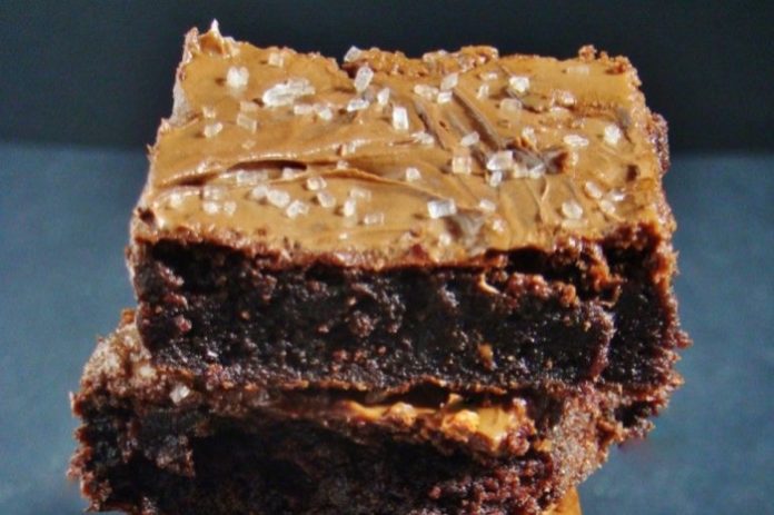 Double chocolate brownie topped with peanut butter frosting and flaky salt crystals on top surface, close-up.