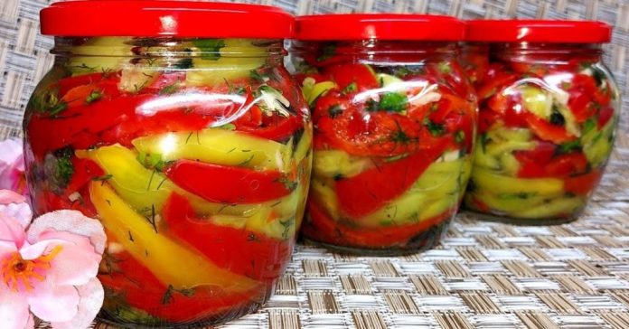 Three glass jars filled with red and yellow pickled peppers and herbs on a woven surface, red lids on top
