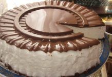 Ჩიტის რძე – კლასიკური რეცეპტი Round chocolate and vanilla cake with white frosting and glossy chocolate ring on a decorative blue plate, a slice removed to reveal the interior.