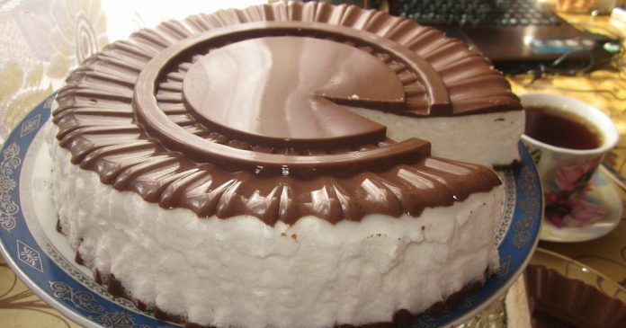 Round chocolate and vanilla cake with white frosting and glossy chocolate ring on a decorative blue plate, a slice removed to reveal the interior.