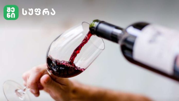 Wine being poured into a glass from a bottle, with a green logo at top-left corner.