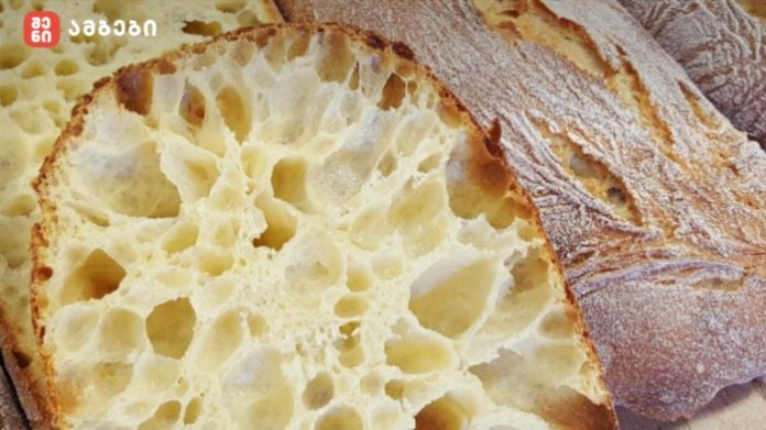 Close-up of a crusty loaf with a pale, airy crumb and large holes inside.
