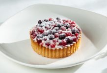 ჯანსაღი ხილის დესერტი Berry tart topped with blueberries and raspberries, lightly dusted with powdered sugar on a white plate.