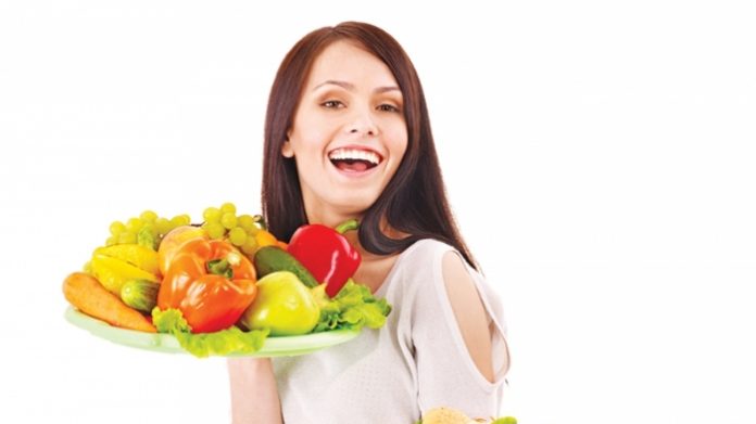 kveba Smiling woman holding a plate of colorful fresh vegetables and fruit.