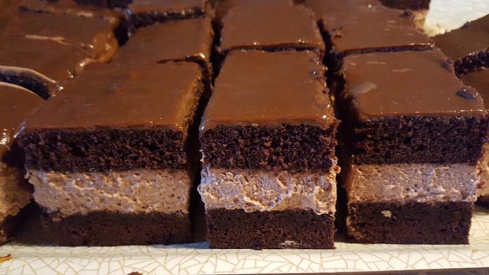 Brownie squares with a dense chocolate base, creamy middle layer, and glossy chocolate top on a plate.
