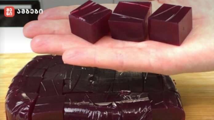 nugbari Hand resting on a glossy, square-cut dark chocolate cake with stacked chocolate blocks on top.