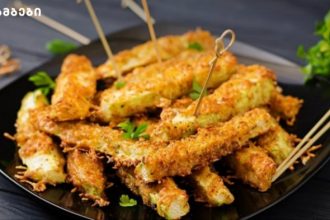 Golden fried zucchini sticks on a black plate, garnished with parsley and skewered with toothpicks.