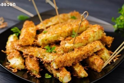 Golden fried zucchini sticks on a black plate, garnished with parsley and skewered with toothpicks.