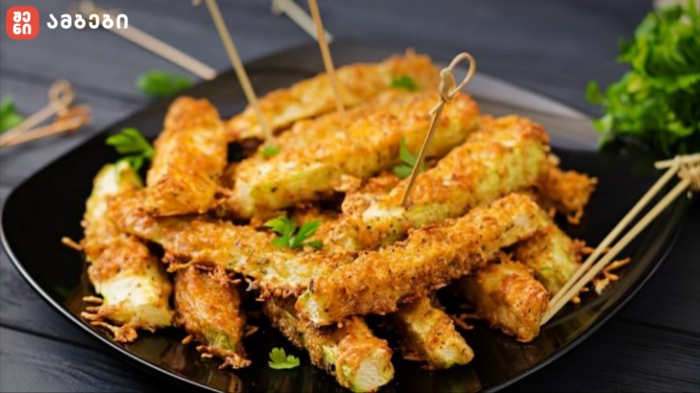 Golden fried zucchini sticks on a black plate, garnished with parsley and skewered with toothpicks.