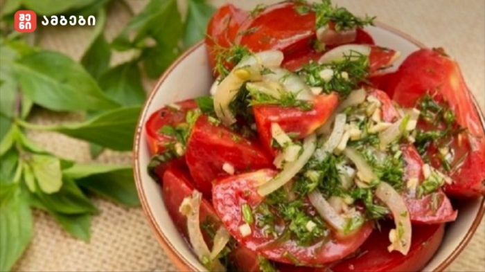 Bowl of chopped tomato salad with onions, dill, and fresh herbs in a ceramic dish.
