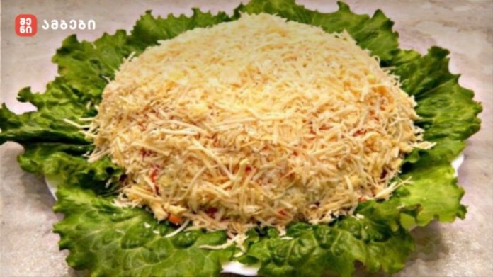 Cheese ball coated in shredded cheese on a bed of green lettuce leaves for serving.