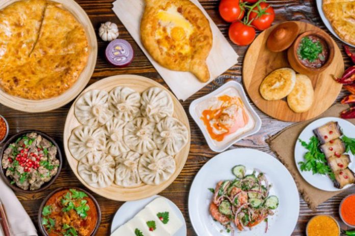 Assorted Asian-inspired dishes on a wooden table: dumplings, curry, bread, fresh tomatoes, and multiple dipping sauces.