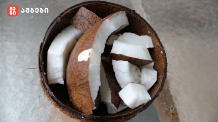 Open coconut with white coconut flesh chunks inside the brown shell on a light surface.