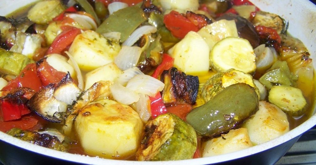 Sautéed vegetables in a pan including potatoes, zucchini, bell peppers, onions, and eggplant.