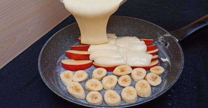 Frying pan with apple wedges and banana coins being coated by thick pancake batter as it’s poured from a ladle, ready to cook.