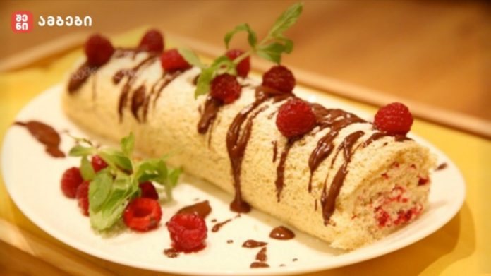 ruleti-shenisupra Rolled sponge cake with raspberries, chocolate drizzle, mint garnish on a white plate.