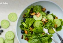 ჩინური კომბოსტოს დიეტური სალათები Green salad with lettuce, cucumber rounds, almonds, and blueberries in a light blue bowl.