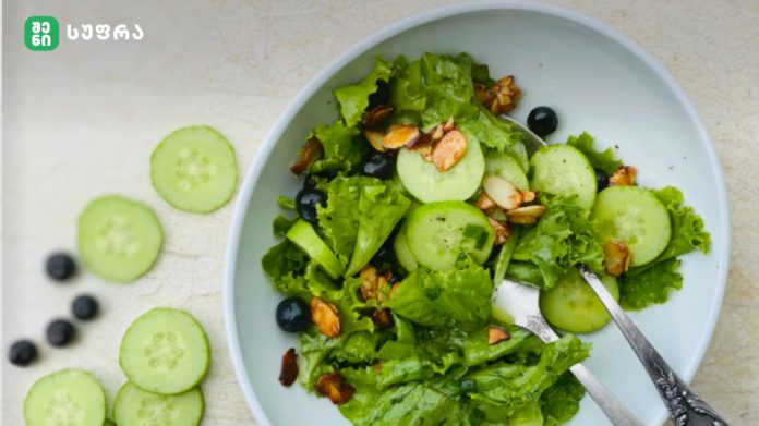 Green salad with lettuce, cucumber rounds, almonds, and blueberries in a light blue bowl.