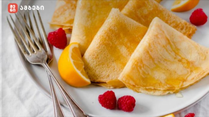 Plate of golden crepes with lemon wedges and raspberries, with forks resting on the plate edge.