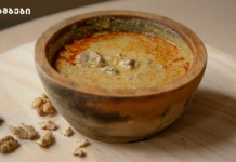 მოამზადეთ აჭარული კერძი – იახნი Rustic clay bowl of creamy walnut soup with paprika oil, on a wooden board with walnut pieces nearby.