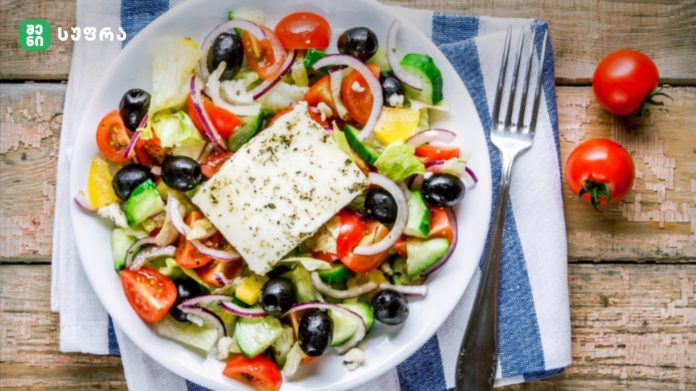 Plate of Greek-style salad with feta cheese, tomatoes, olives, cucumbers, and red onions on a wooden table.
