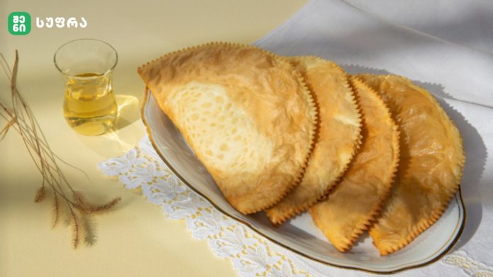Plate of golden pastries on a decorative plate with a glass of pale golden liquid nearby on a pale yellow table.