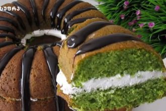 Ring-shaped cake with pistachio-green layers, white cream filling, and glossy chocolate drizzle.
