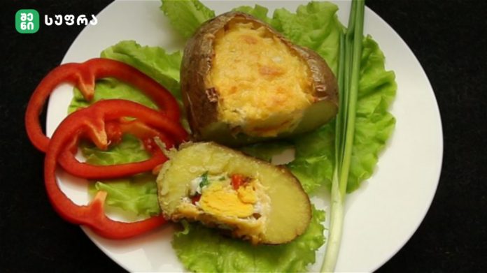 Plate with two baked stuffed potatoes topped with melted cheese, set on a bed of lettuce with red bell pepper rings and green onions nearby.