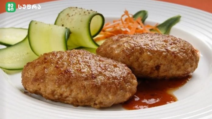 Two browned fried meat croquettes with a red sauce on a white plate, beside cucumber ribbons and shredded carrot.