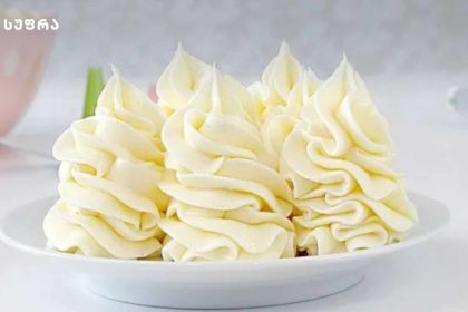 White frosted cake piled with piped rosette buttercream decorations on a white plate.