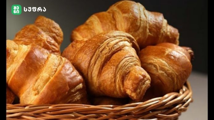 Pile of golden-brown croissants in a wicker basket with a dark background in the backdrop.