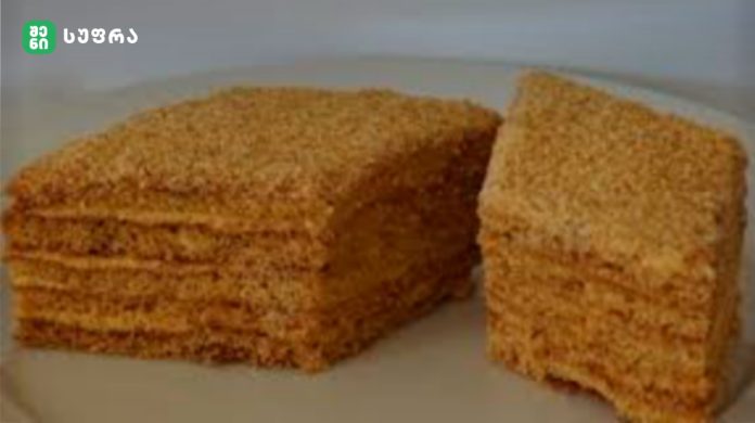 Two slices of dense brown loaf on a plate, crumbly texture visible, with a logo in the top-left corner.