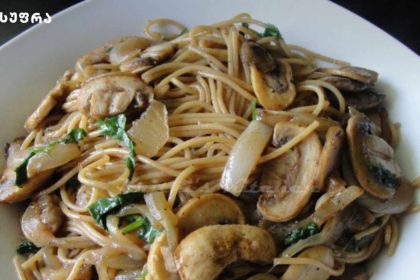 Plate of spaghetti with mushrooms and greens on a white dish.