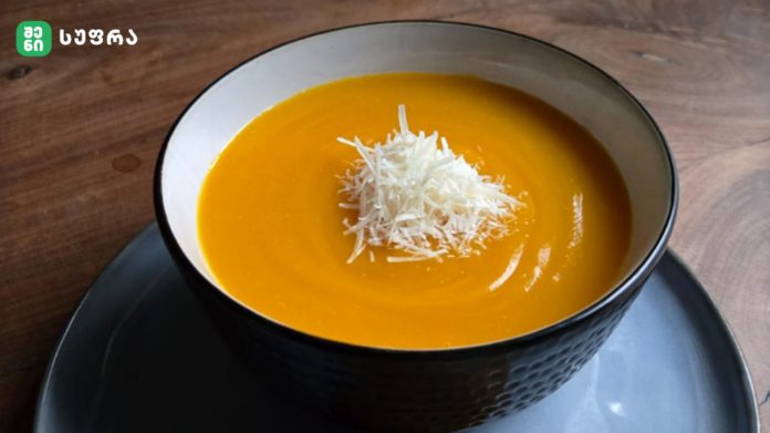 Creamy orange pumpkin or carrot soup in a white-rimmed bowl, topped with shredded coconut
