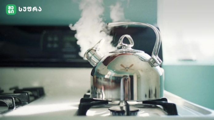 Shiny chrome kettle boiling on a gas stove with steam rising from the spout in a kitchen.