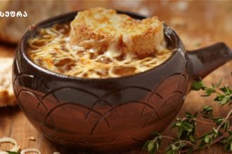 Warm bowls of French onion soup in a rustic brown pot topped with melted cheese and a crusty crouton, with thyme nearby.