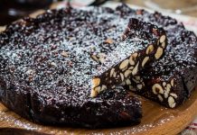 “სიენური პანფორტე”-ტრადიციული კერძი Dense chocolate loaf cake studded with almonds, sliced to reveal a rich interior, lightly dusted with powdered sugar on a wooden board.