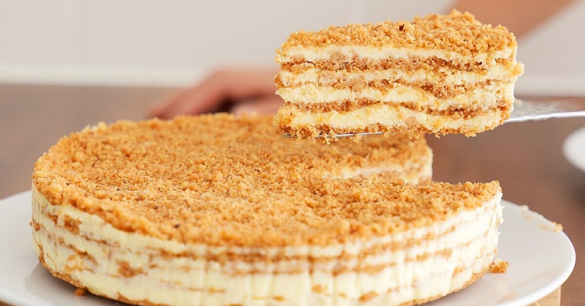 Layered crumb cake with a creamy filling on a white plate, a slice being lifted with a spatula.