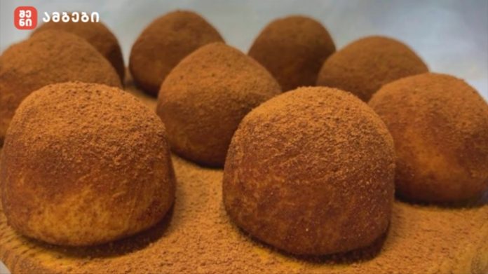 tiramisu Close-up of round chocolate truffles dusted with cocoa powder, arranged on a wooden surface with a red logo in the corner.